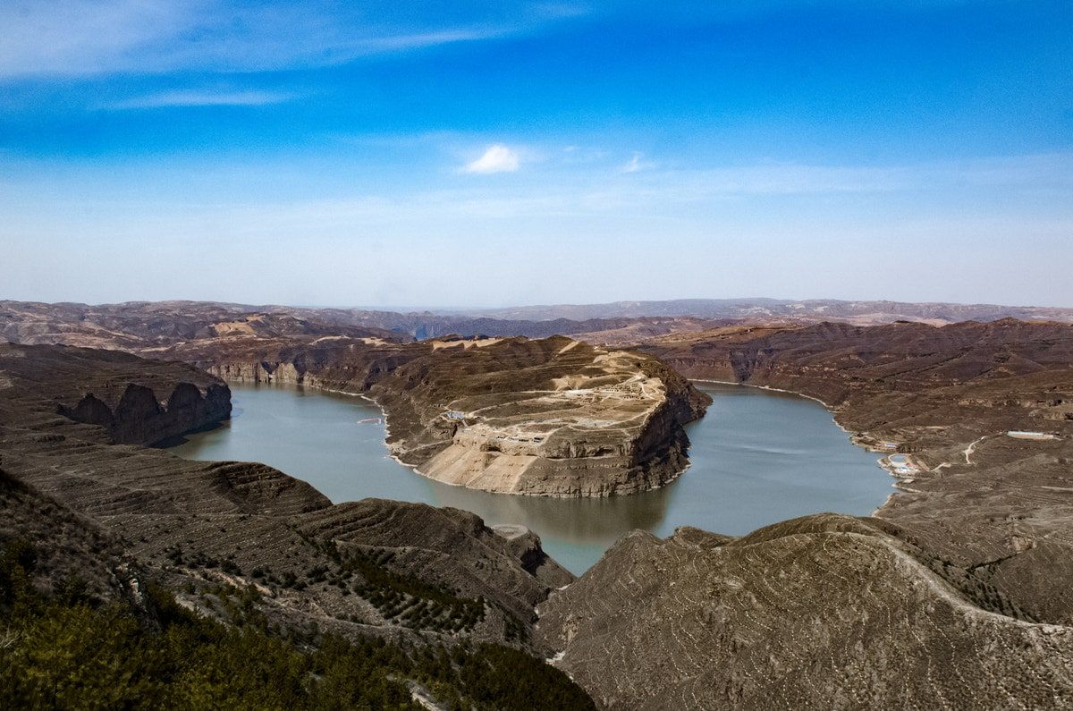 The Yellow River looping around a terraced spur in bare loess hills, under a blue sky