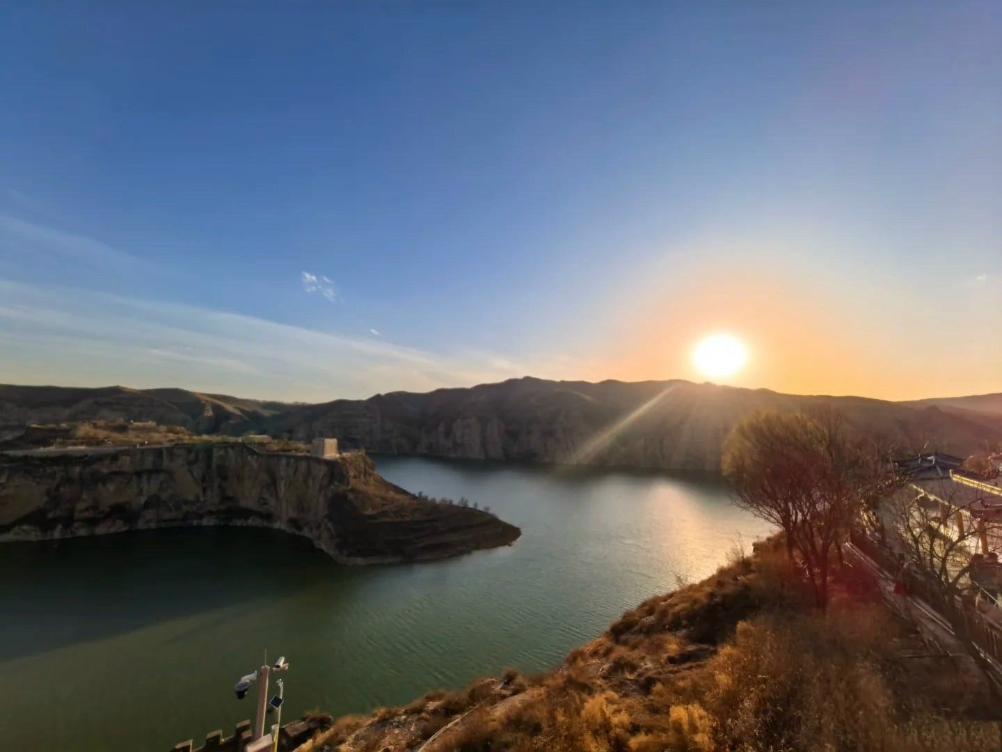 The sun setting over the green Yellow River at Laoniuwan, a small stone tower on the clifftop across the bend