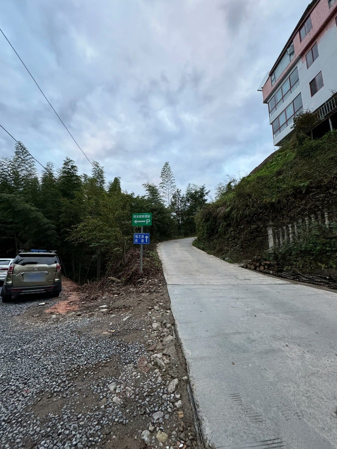 Eine Betonstraße durch Zhongliu mit parkenden Autos links, wo der Pfad nach Ping’an hinabführt