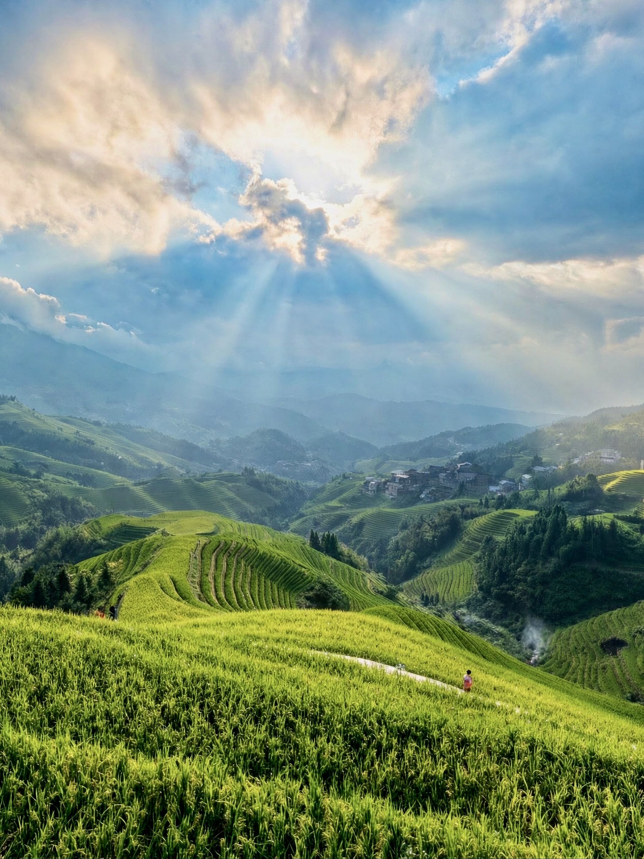 Sonnenstrahlen brechen durch die Wolken über grünen Reisterrassen und einem langen Tal