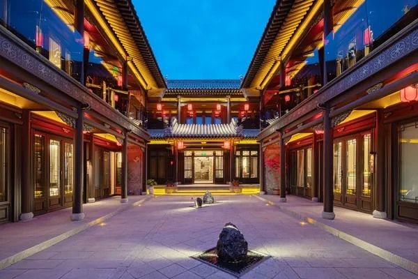 The lantern-lit courtyard of Bo Yuan'er at dusk, two storeys of carved wooden galleries around a stone yard