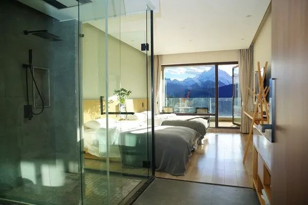 A room at Snow Mountain Wake Up Hotel seen past its glass shower, the window wall onto the snow peaks