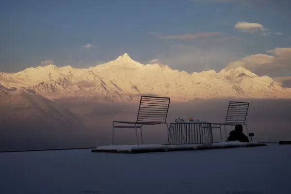 Chairs on the terrace of Snow Mountain Wake Up Hotel, facing the Meili peaks lit pink and gold at sunrise