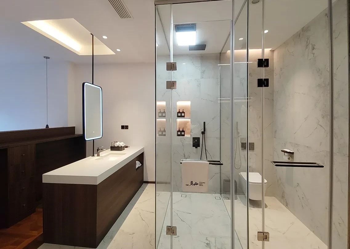 The bathroom at Yulong Mountain View Homestay: a long washstand and a marble walk-in shower behind glass