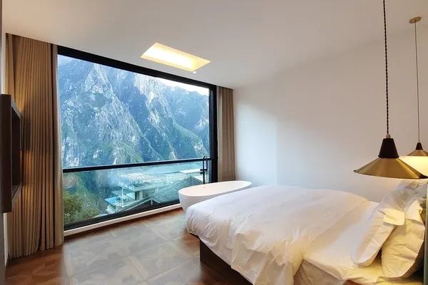 A room at Yulong Mountain View Homestay: the bed and a freestanding bathtub before a window wall onto the gorge's cliffs