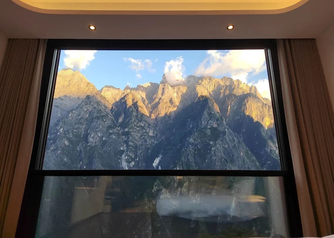 The peaks across the gorge lit gold by a low sun, framed by a window at Yulong Mountain View Homestay