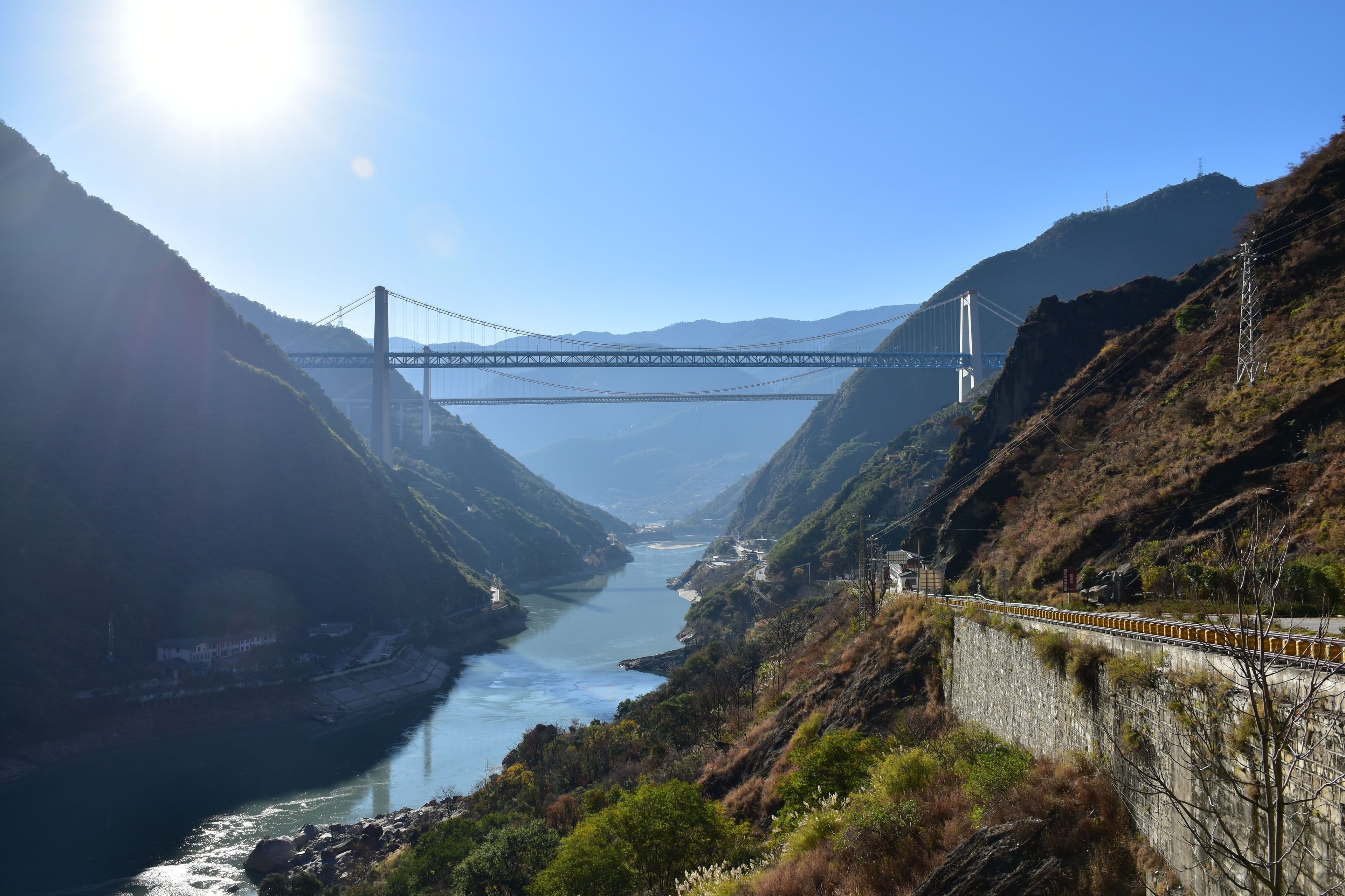 Two suspension bridges, one behind the other, spanning Tiger Leaping Gorge high above the Jinsha River, against the afternoon sun