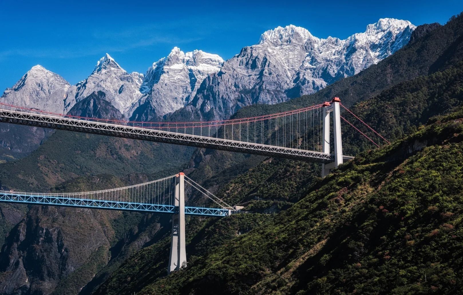 Deux ponts suspendus franchissent les gorges du Saut du Tigre sous les sommets enneigés du Dragon de Jade, ciel d’un bleu profond