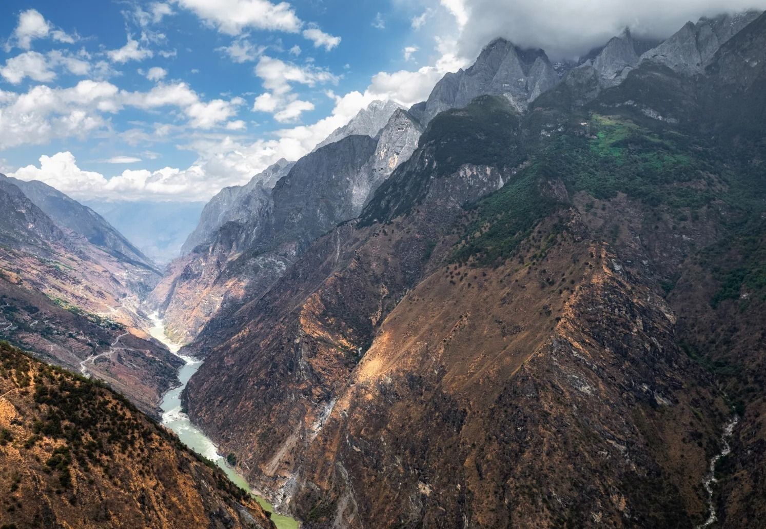 Plongée dans les gorges du Saut du Tigre : tout en bas, le Jinsha vert pâle entre des pentes brunes et raides, des sommets gris qui se perdent dans les nuages