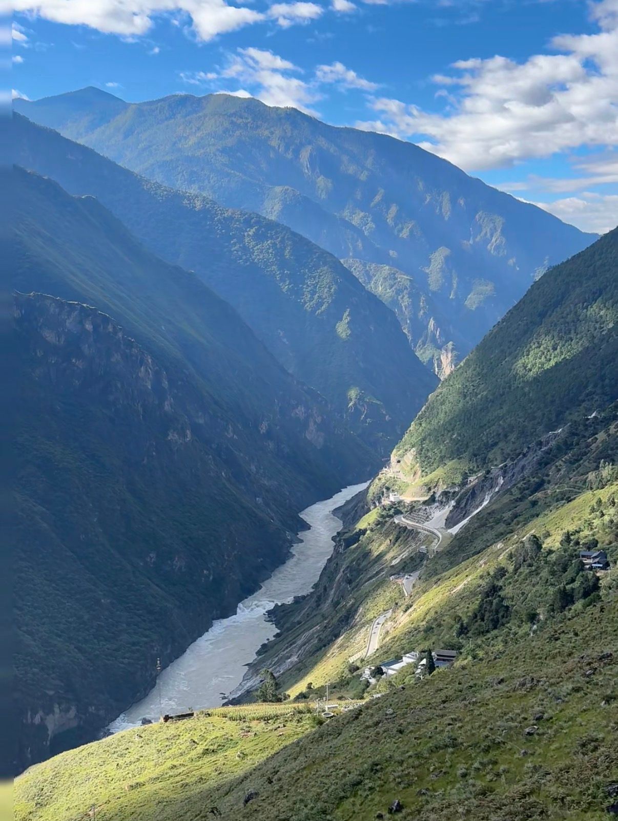 The Jinsha River winding through Tiger Leaping Gorge under a blue sky, seen from high above, with the road and village houses on the slope