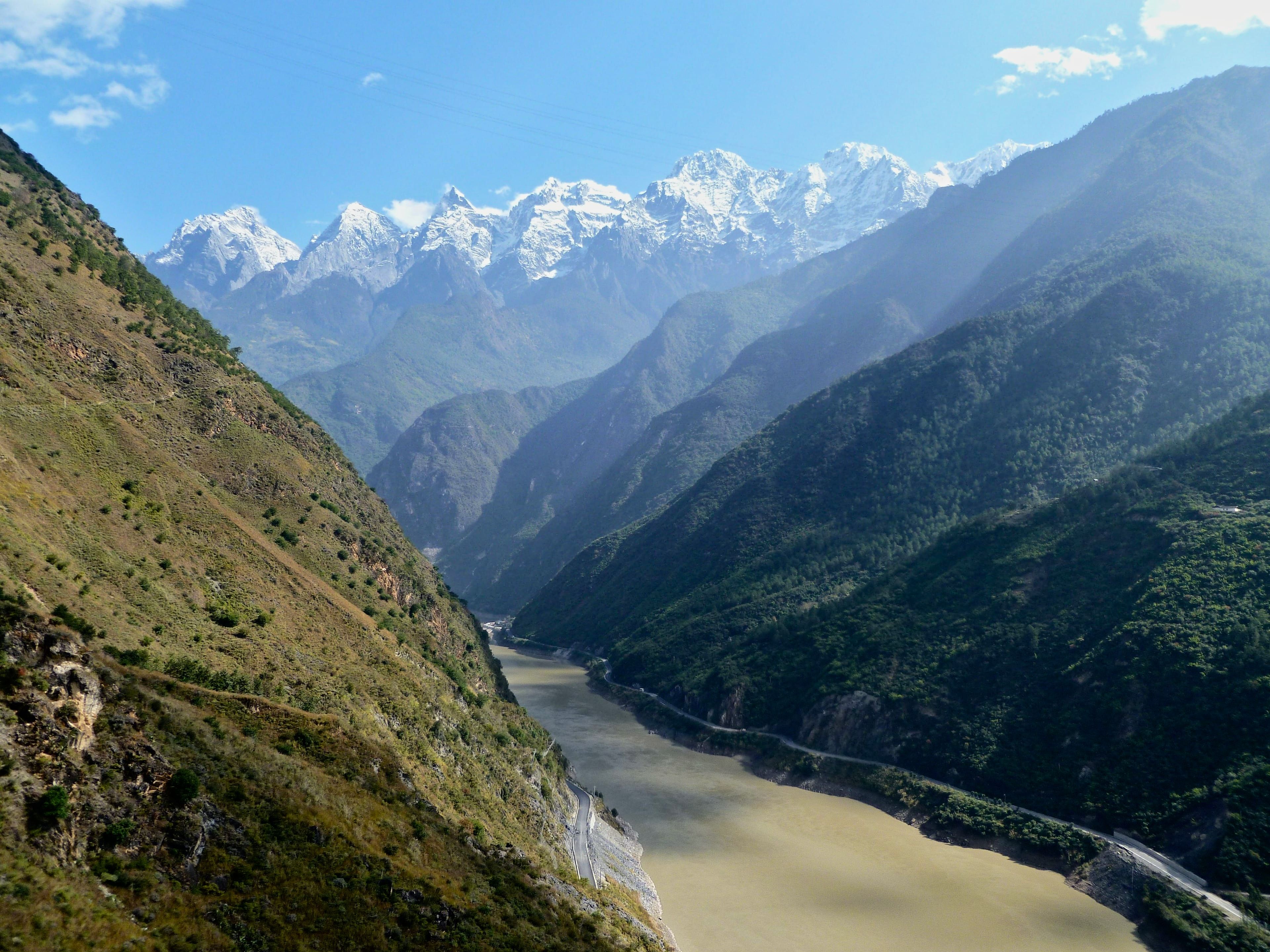The silt-brown Jinsha River and the road along its bank deep in Tiger Leaping Gorge, the snow peaks of Jade Dragon Snow Mountain at the head of the valley
