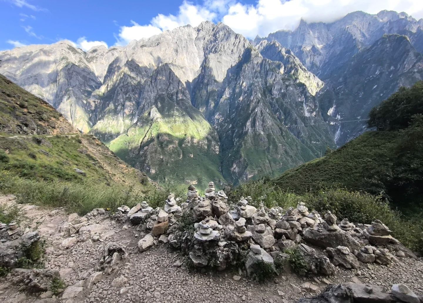 De petits tas de pierres mani sur le sentier du haut, face aux falaises grises du Dragon de Jade de l’autre côté des gorges, sous un ciel bleu et des nuages blancs