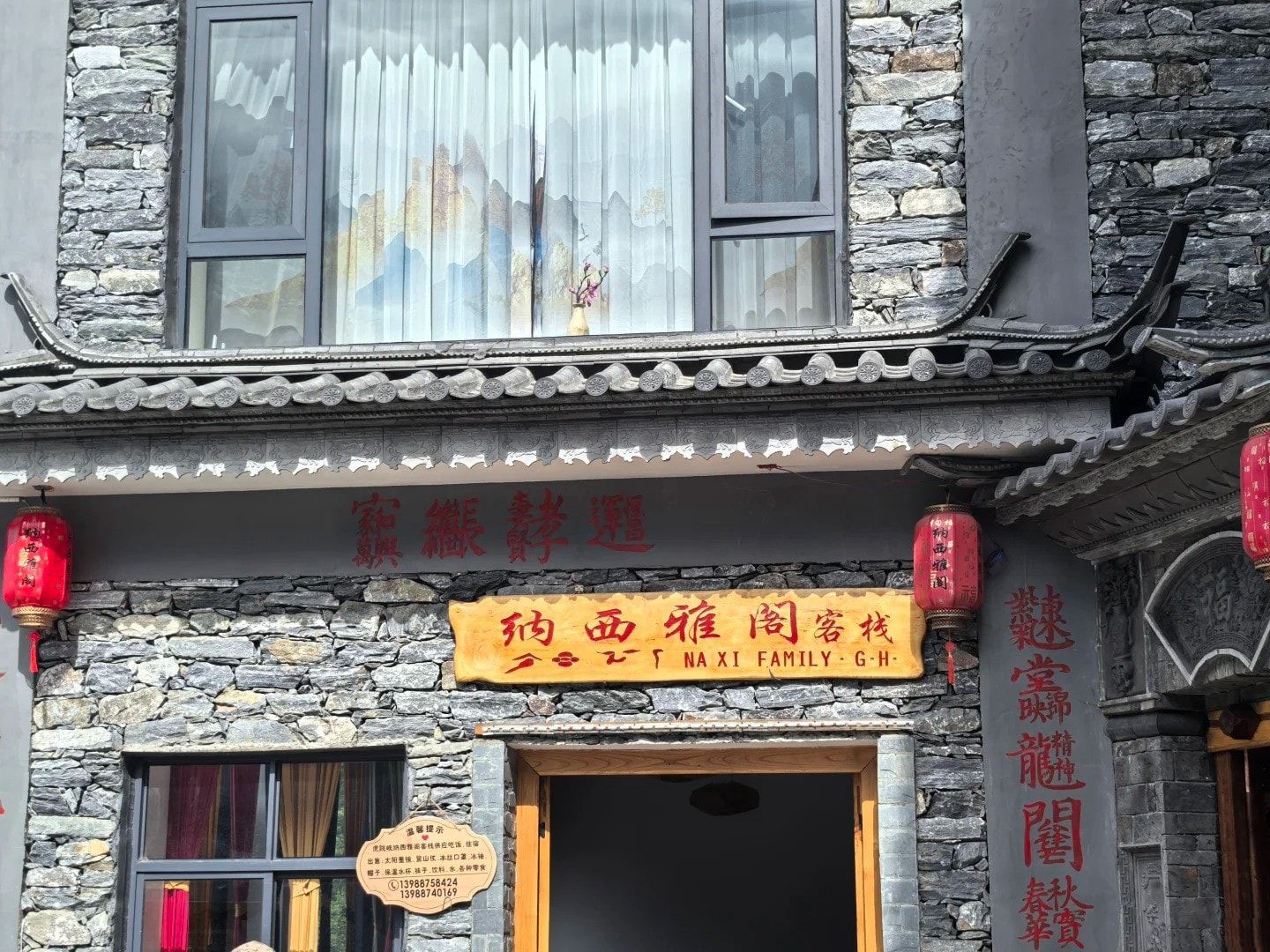 La façade de la Naxi Family Guesthouse, avec ses murs de pierre grise, ses lanternes rouges et son enseigne dorée