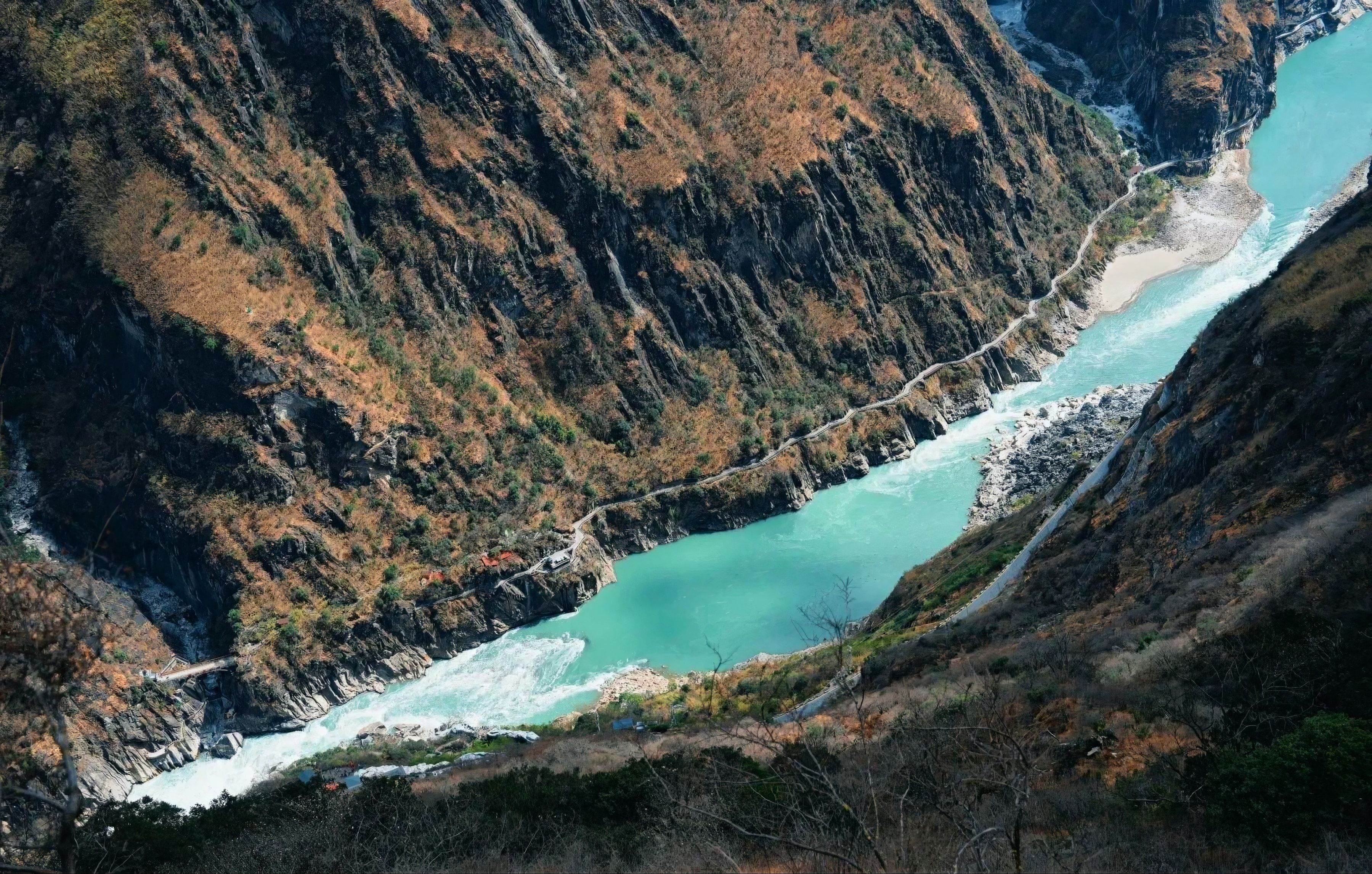Looking down on a bend of the turquoise Jinsha River, a path cut into the cliffs along the far bank