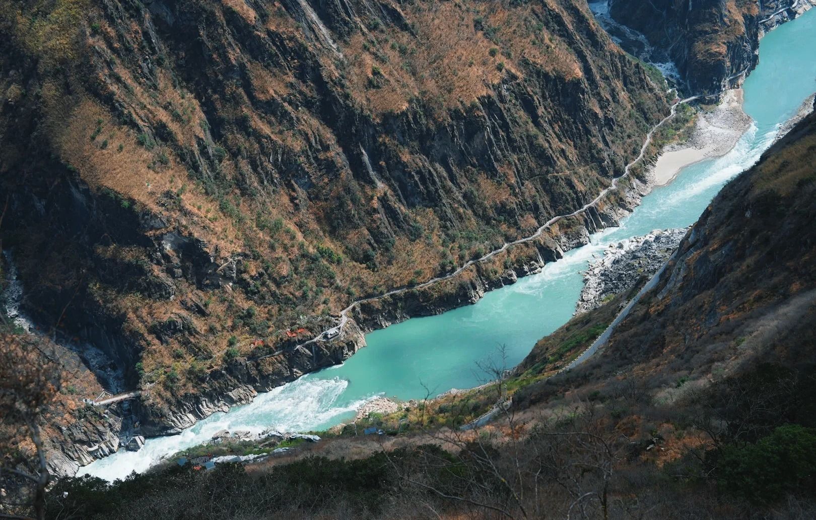 Vue plongeante sur un coude du Jinsha turquoise, avec un sentier taillé dans la falaise le long de l’autre rive