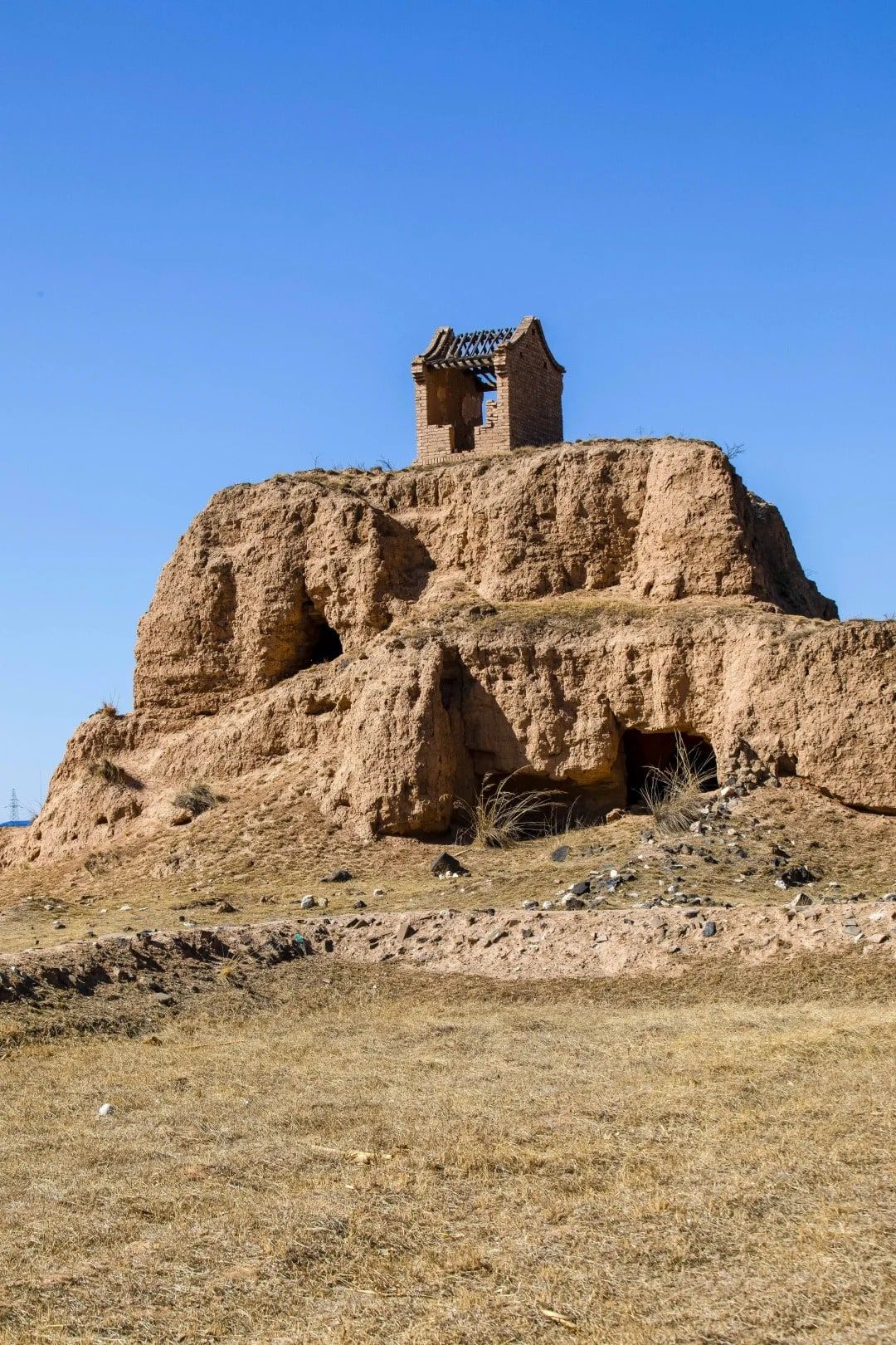 A small brick shrine on top of a crumbling earthen watchtower, under a deep blue sky