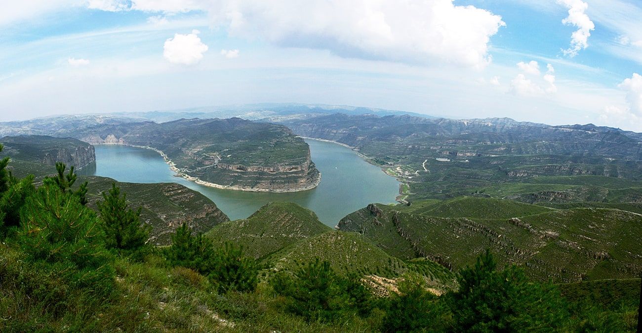The Yellow River sweeping in a wide bend between green hills, seen from a pine-edged hilltop