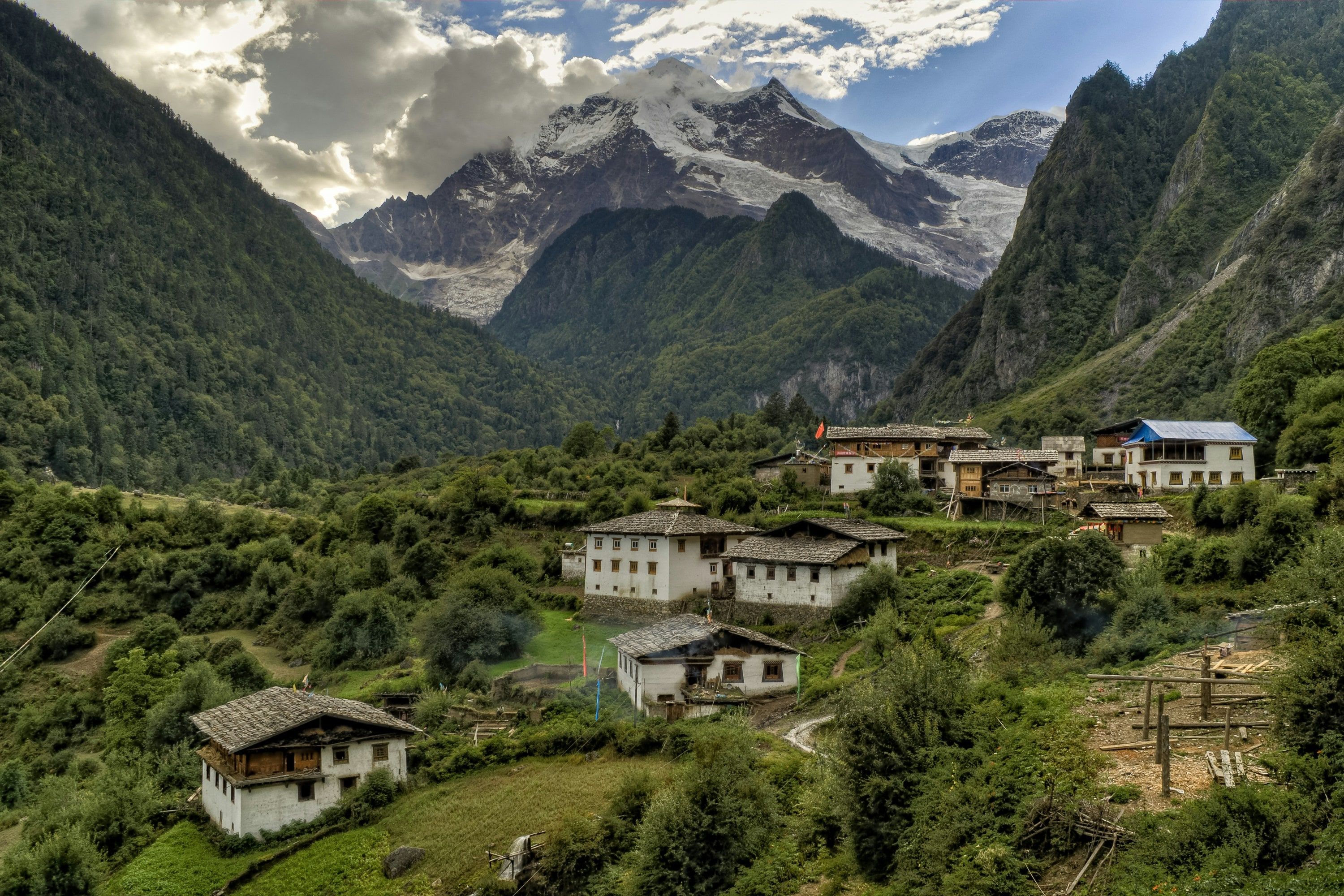 Whitewashed Tibetan houses with grey roofs among fields and trees in Upper Yubeng, a glaciated snow peak in cloud at the head of the valley