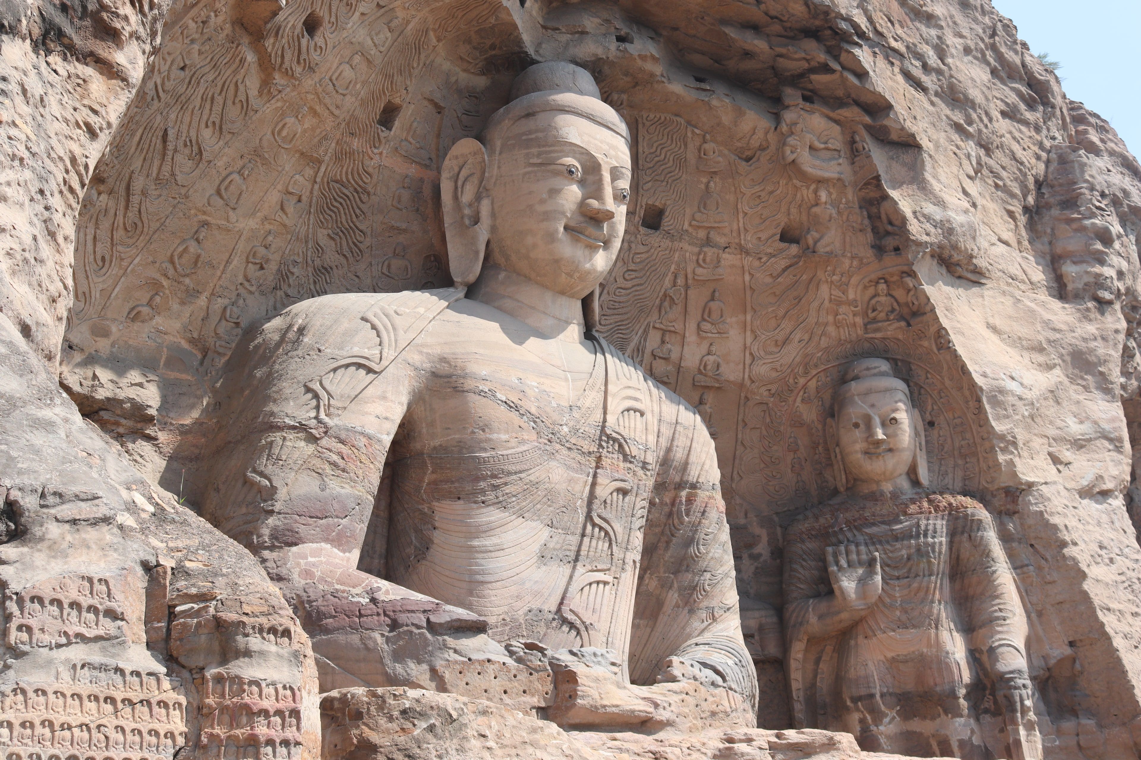The great seated Buddha of Cave 20 at Yungang, carved into warm sandstone, with a standing Buddha at his side