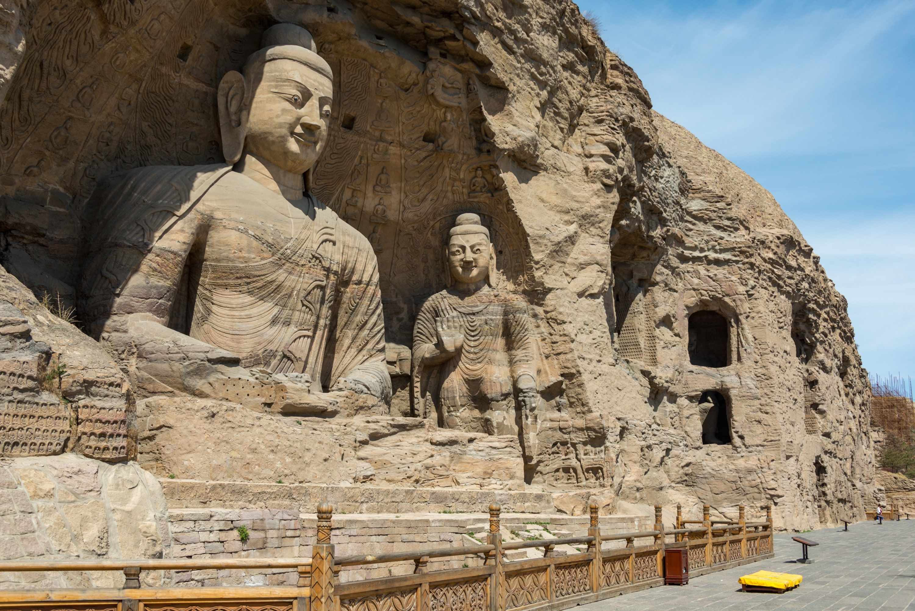The seated and standing Buddhas of Cave 20 at Yungang above a wooden railing, under a blue sky